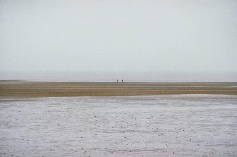 two people walking on a beach far away. Shot on a prime lens