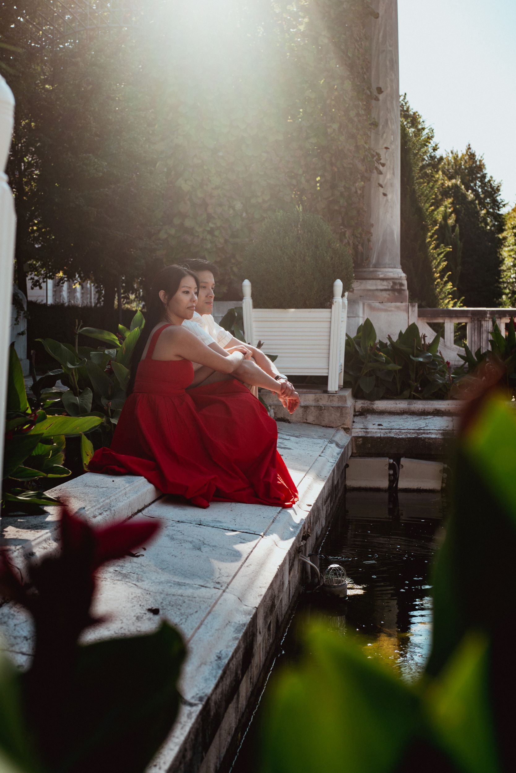 Love story photography in Vienna – cinematic couple portrait of the two sitting by a pond in Volksgarten
