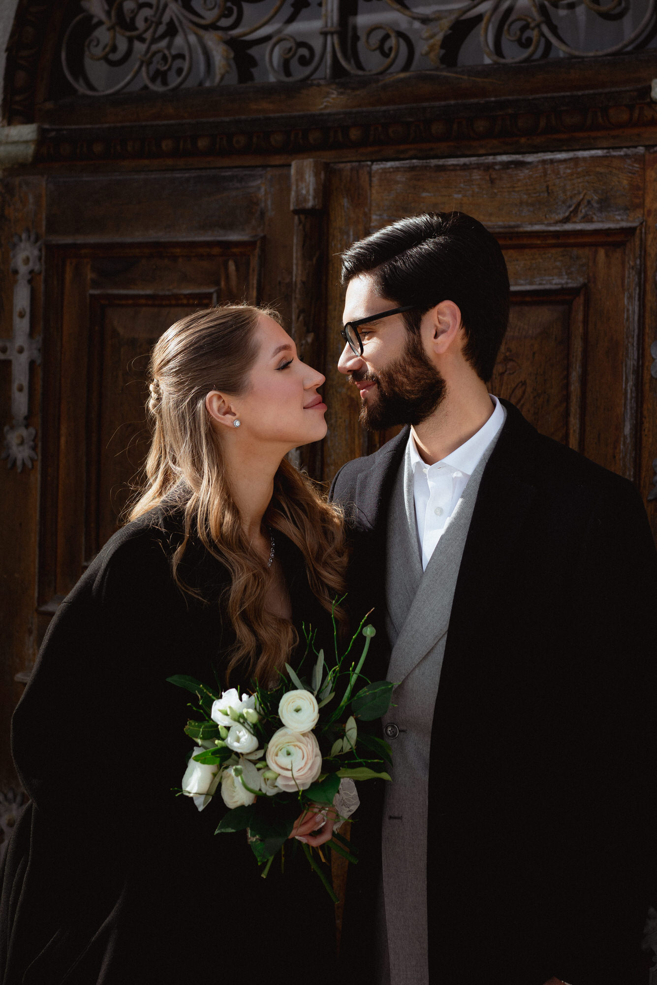 groom and bride looking at each other in front of an entrance to a chirch